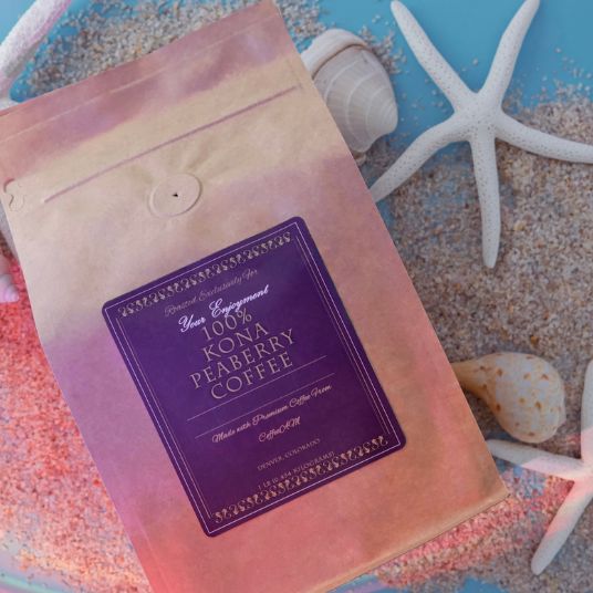 Coffee package with a purple label on a sandy surface with starfish and shells.