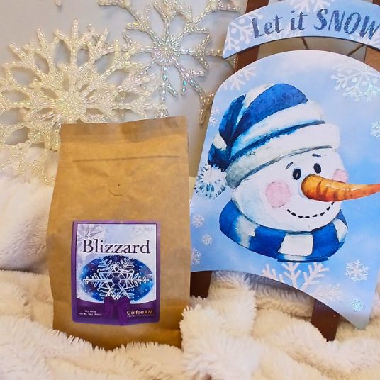 Bag of 'Blizzard' coffee and a snowman-themed card with 'Let it Snow' text on a fluffy white background.