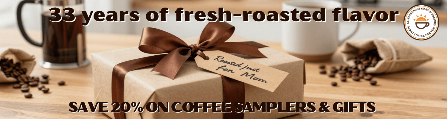 A wrapped coffee gift box with a large brown ribbon sits on a wooden surface with coffee beans, mugs, and a small burlap sack in the background. Text across the top reads '33 years of fresh-roasted flavor' and the bottom reads 'SAVE 20% ON COFFEE SAMPLERS & GIFTS'.