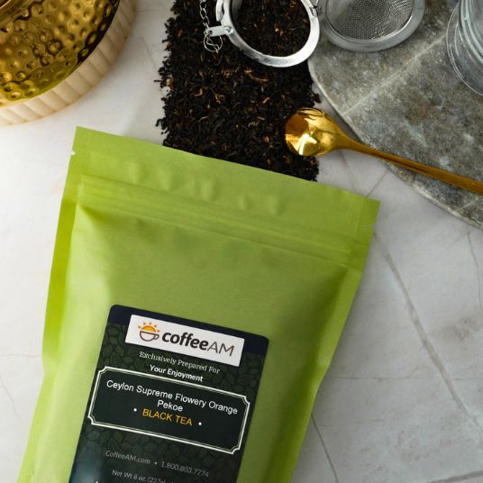 Green tea package with 'coffeeAM' label on a white surface with tea-making items.