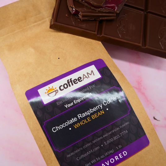 CoffeeAM chocolate raspberry coffee package on a pink surface with chocolate bars.