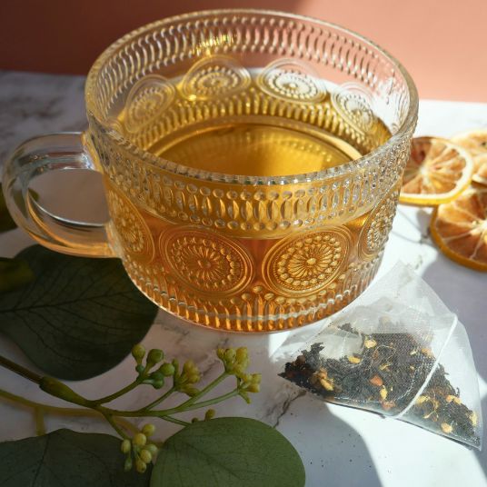 Decorative glass mug filled with tea on a marble surface with dried oranges and tea leaves.