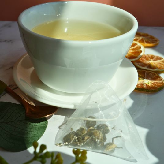 White teacup with tea and a tea bag on a saucer, with dried oranges in the background.
