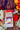 A kraft paper bag of CoffeeAM "Cranberry Cream" flavored coffee positioned against an autumn-themed background featuring colorful orange and red leaves, cinnamon sticks, dried orange slices, and small festive white berry accents.