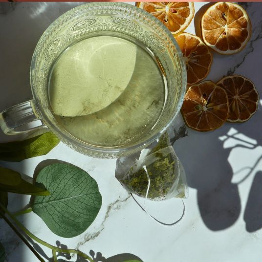 Clear glass mug with tea, a tea bag, and dried orange slices on a marble surface.