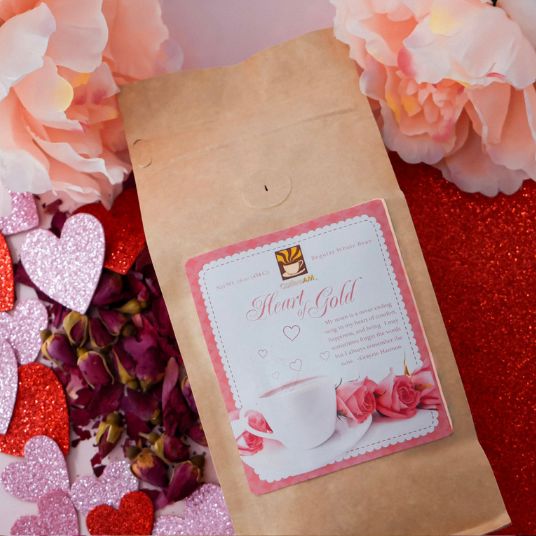 Kraft paper coffee bag with 'Heart of Gold' label surrounded by flowers and decorative hearts on a red background