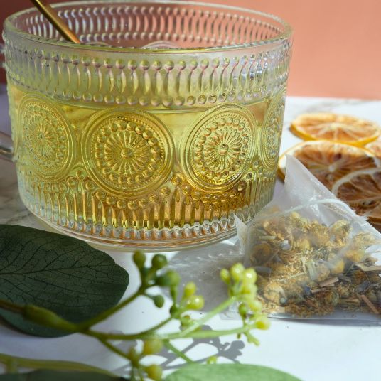 Decorative glass container with floral patterns on a table with dried flowers and leaves.