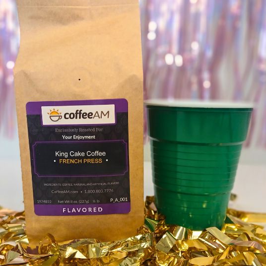 CoffeeAM King Cake Coffee package with a green cup and gold tinsel on a blurred background