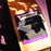 A brown kraft-paper bag of coffeeAM Maple Bacon Coffee (Drip Grind) in bright, direct sunlight, casting strong leaf-shaped shadows across the bag and purple background.