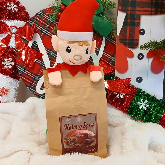 Elf plush toy on a Nutmeg Spice coffee bag with Christmas decorations in the background