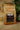 A kraft paper bag of CoffeeAM Organic Nicaragua 'Ceocafen' Whole Bean coffee, set against a burlap background with green leafy houseplants. The label displays the CoffeeAM logo, USDA Organic seal, and reads 'ORGANIC FAIR-TRADE'.