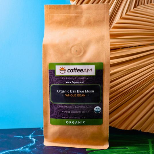 CoffeeAM Organic Bali Blue Moon coffee package on a textured surface with a blue gradient background