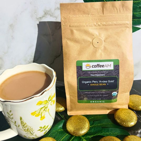 CoffeeAM Organic Peru 'Andes Gold' coffee package with a cup of coffee and gold cookies on a green leafy background.