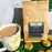 CoffeeAM Organic Peru 'Andes Gold' coffee package with a cup of coffee and gold cookies on a green leafy background.