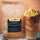 A bag of Coffee AM Spirit Revive Iced Coffee Blend Espresso stands next to a tall glass of iced coffee with a small yellow floral paper umbrella, against a peach-colored background.