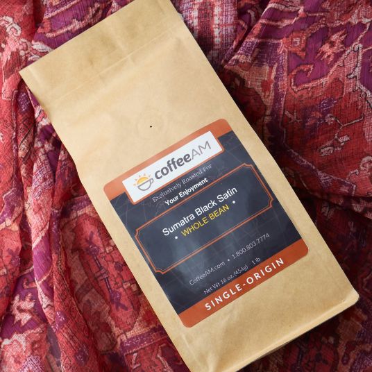 CoffeeAM Sumatra Black Satin coffee package on a patterned fabric background