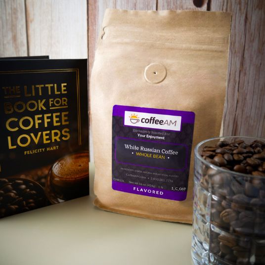 Coffee bag with a label, glass of coffee beans, and book titled 'The Little Book for Coffee Lovers' on a wooden surface.